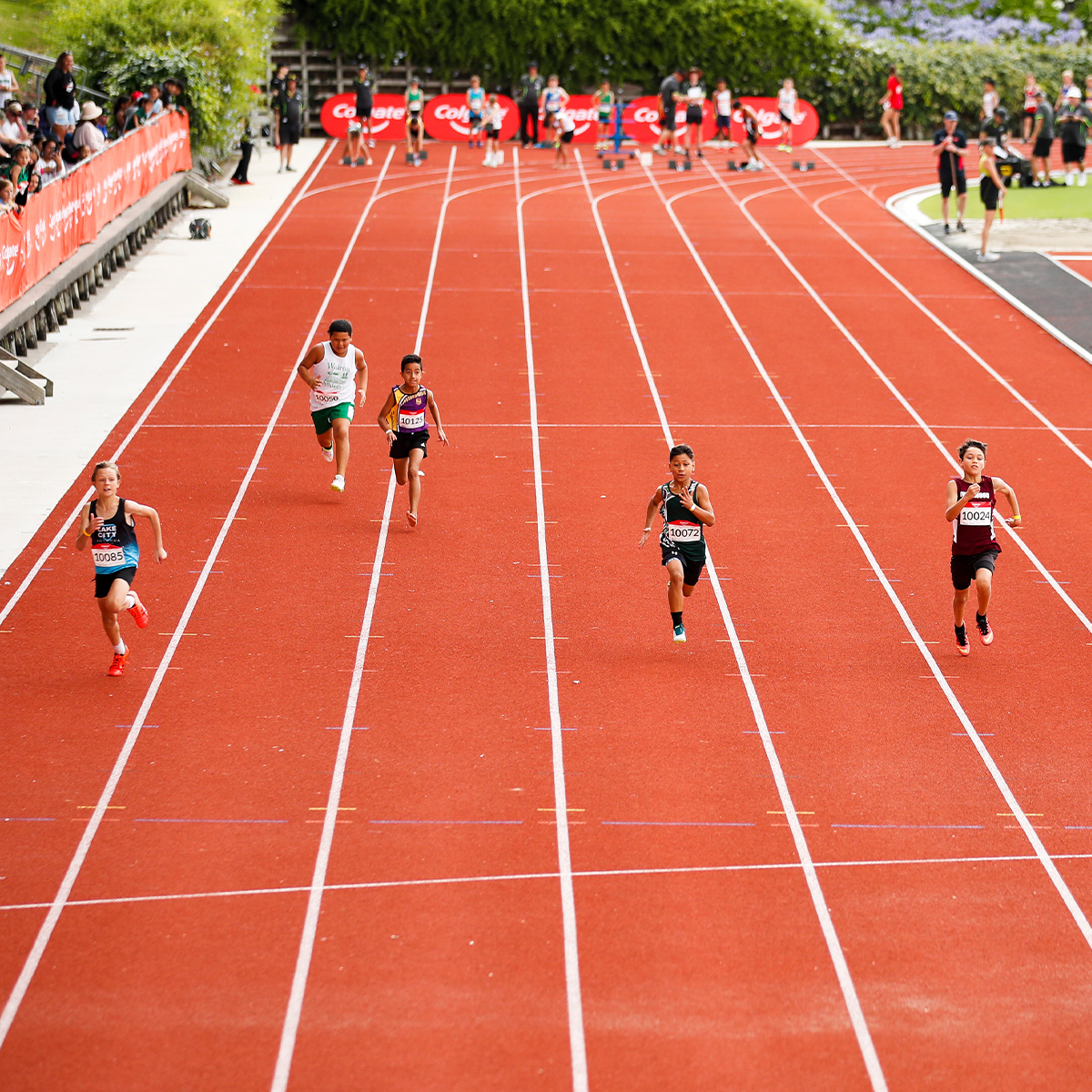 Children running towards the camera on a red running track from an elevated vantage point.